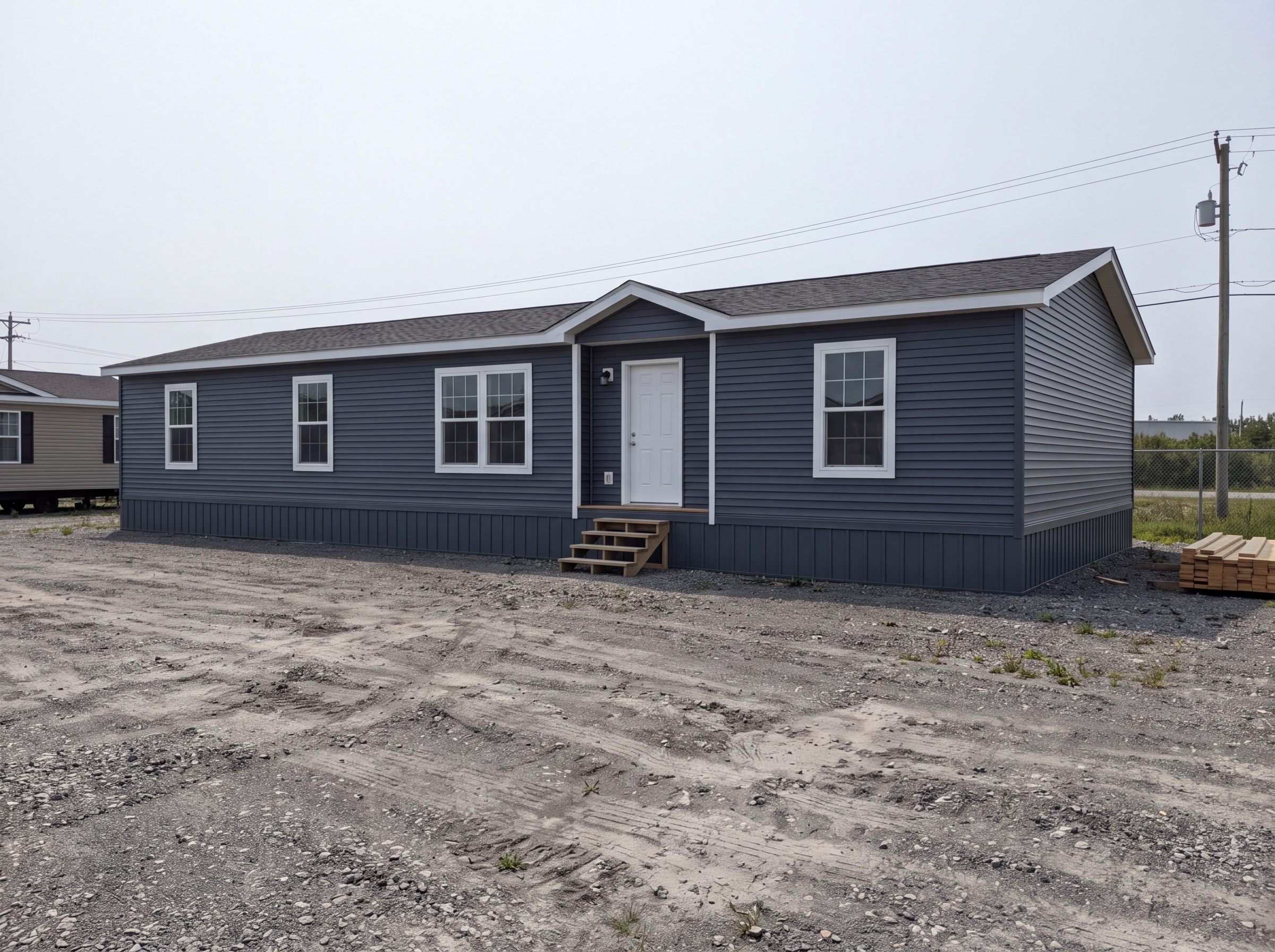 Original photo: slate-blue manufactured home on a gravel factory lot